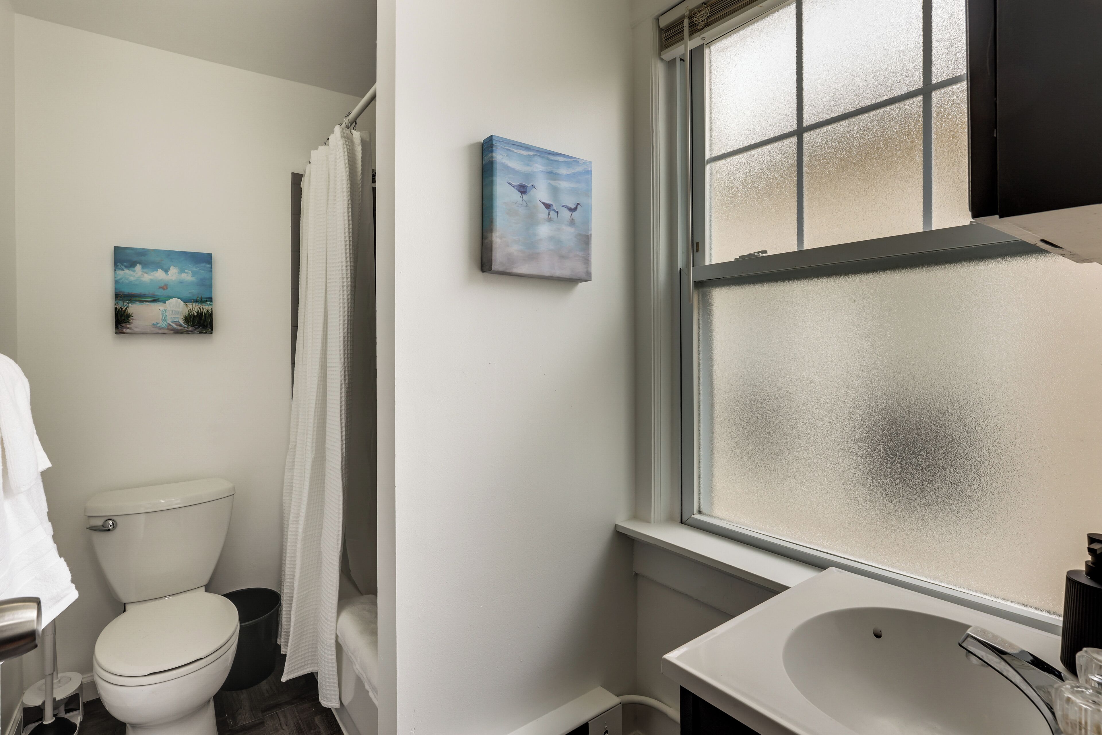 A bathroom with a toilet, a sink, and a frosted window.