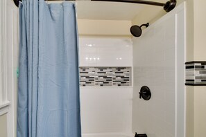A shower area with a blue shower curtain, a handheld showerhead, and a tiled wall with a black and white pattern.