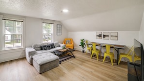 A living room with a sofa, ottoman, coffee table, and yellow chairs. - Extended-stay Apartment in Downtown MC Near Lake (Michigan City)