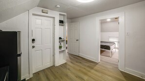 A room with a bed, a white door, a white ceiling fan, and a wooden floor. - Extended-stay Apartment in Downtown MC Near Lake (Michigan City)
