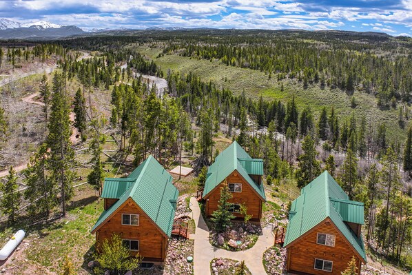 A lodge with three cabins, surrounded by a forest and mountains.