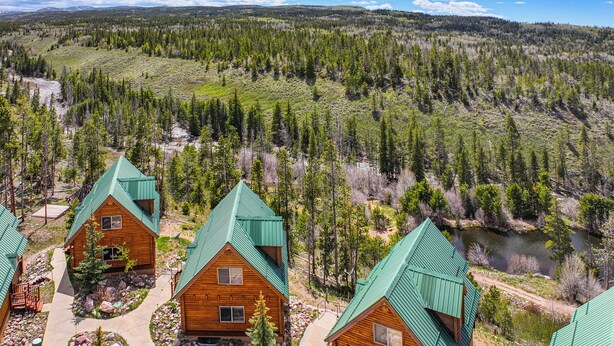 A lodge with multiple cabins, each with a green roof, surrounded by a forested landscape and a river. - Hike, Fish & Ride Atvs! Forest-view Unit in Kamas (Evanston)