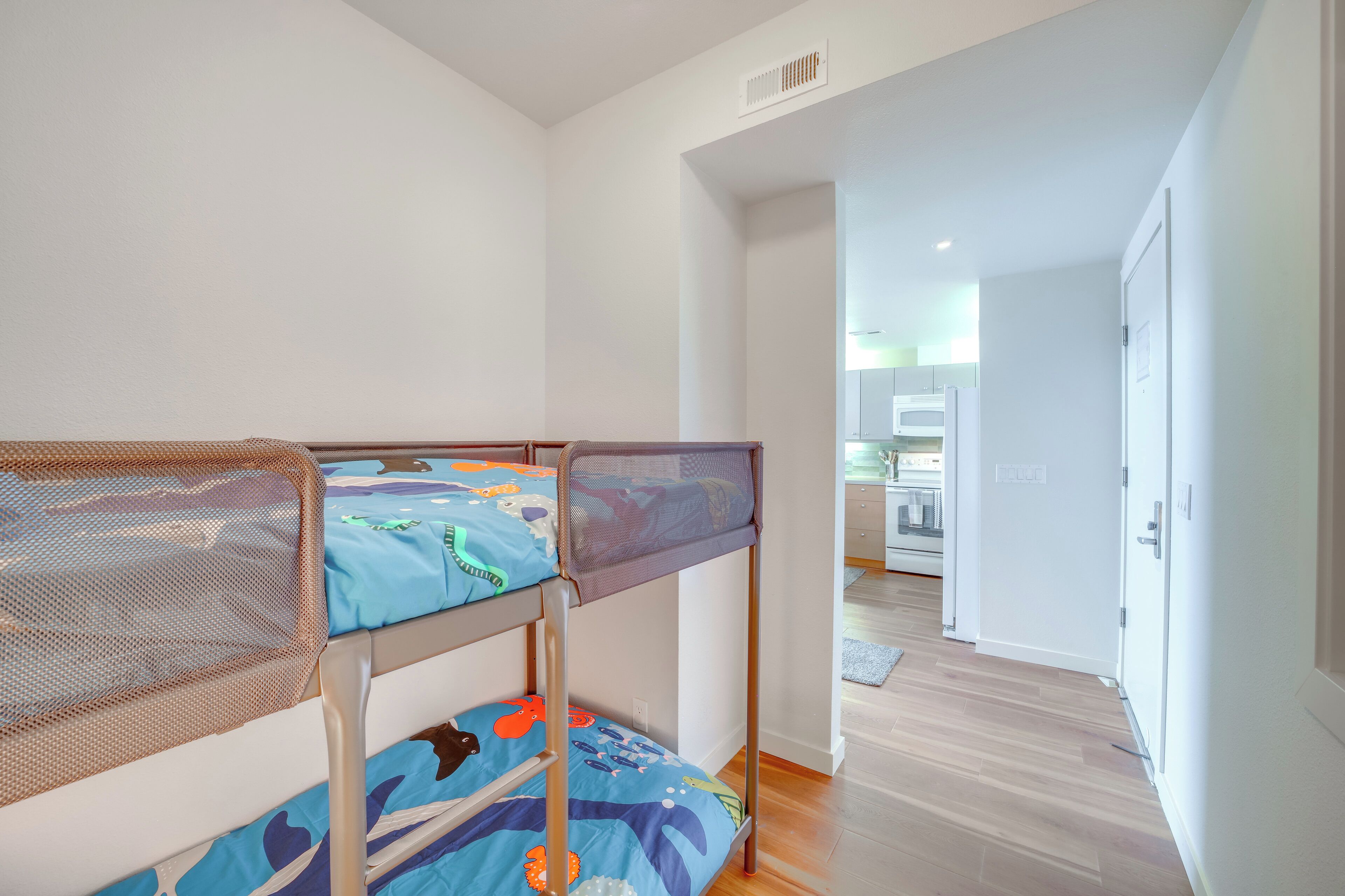A bunk bed with a mesh headboard, a kitchen area in the background, and a wooden floor.