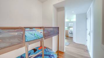 A bunk bed with a mesh headboard, a kitchen area in the background, and a wooden floor.