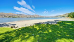 A beach with clear skies, a grassy foreground, and distant hills. - Dual Chelan Resort Suites: Pool, Hot Tub & Beach (Chelan)