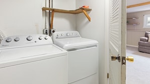 Ein Waschbereich mit einer Whirlpool Waschmaschine und einem Trockner, einem Holzregal und einer Tür mit einer Messingklinke.