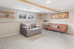 A room with a grey sofa, a brown leather sofa, a window, and a wall-mounted artwork.