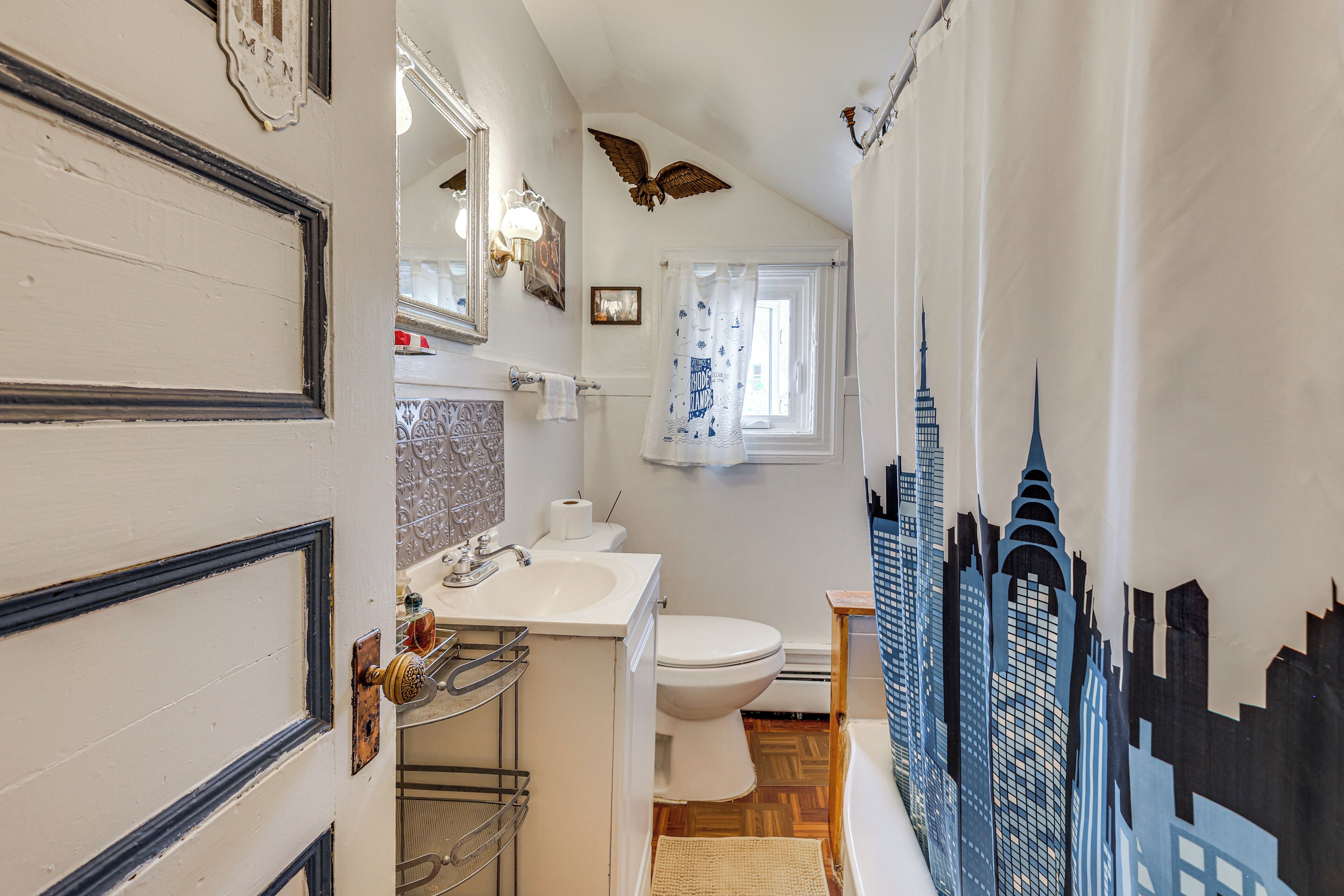 Une salle de bain équipée de toilettes, d’un lavabo et d’un rideau de douche orné d’un motif représentant un paysage urbain.