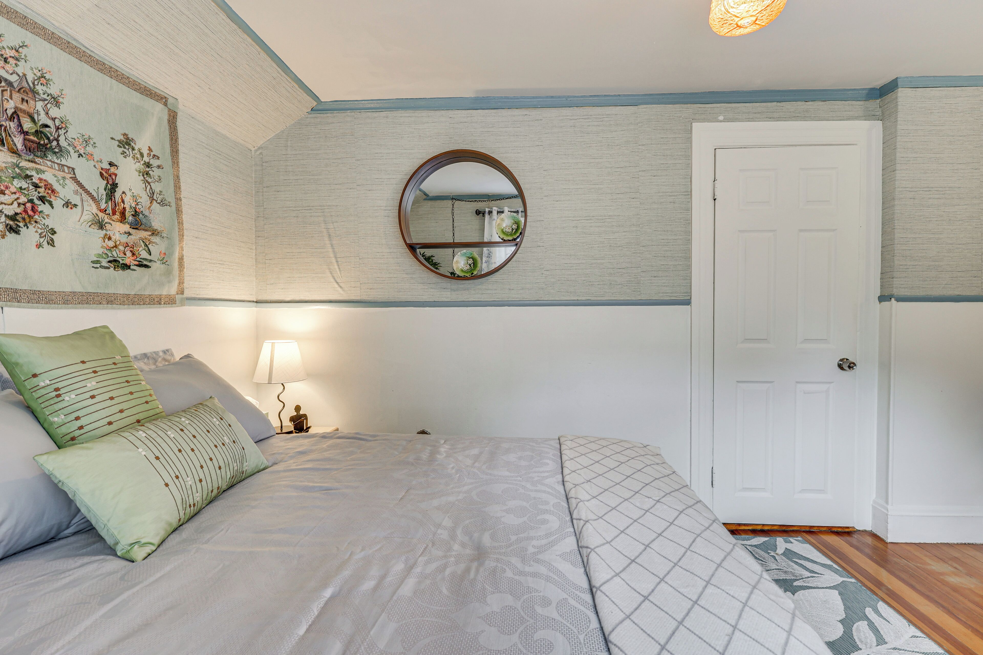 Un dormitorio con una cama, un espejo, una puerta y una pared decorada con un tapiz floral.