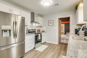 A modern kitchen with stainless steel appliances, white cabinetry, and a marble countertop. - 2 Mi to OKC Fairgrounds: Pet-friendly Home w/ Yard (Oklahoma City)