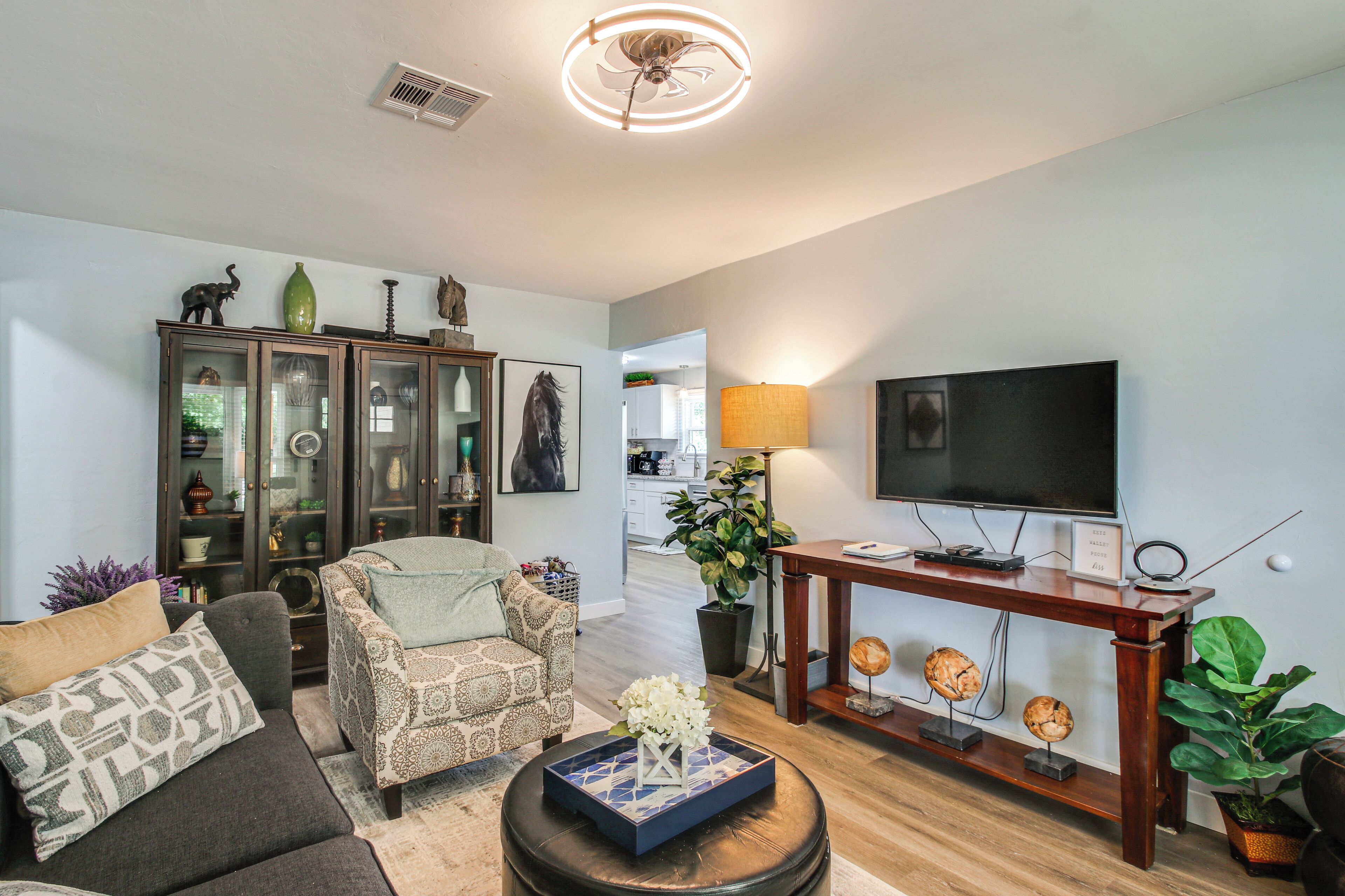 A living room with a sofa, armchair, TV, and a cabinet with glass doors.