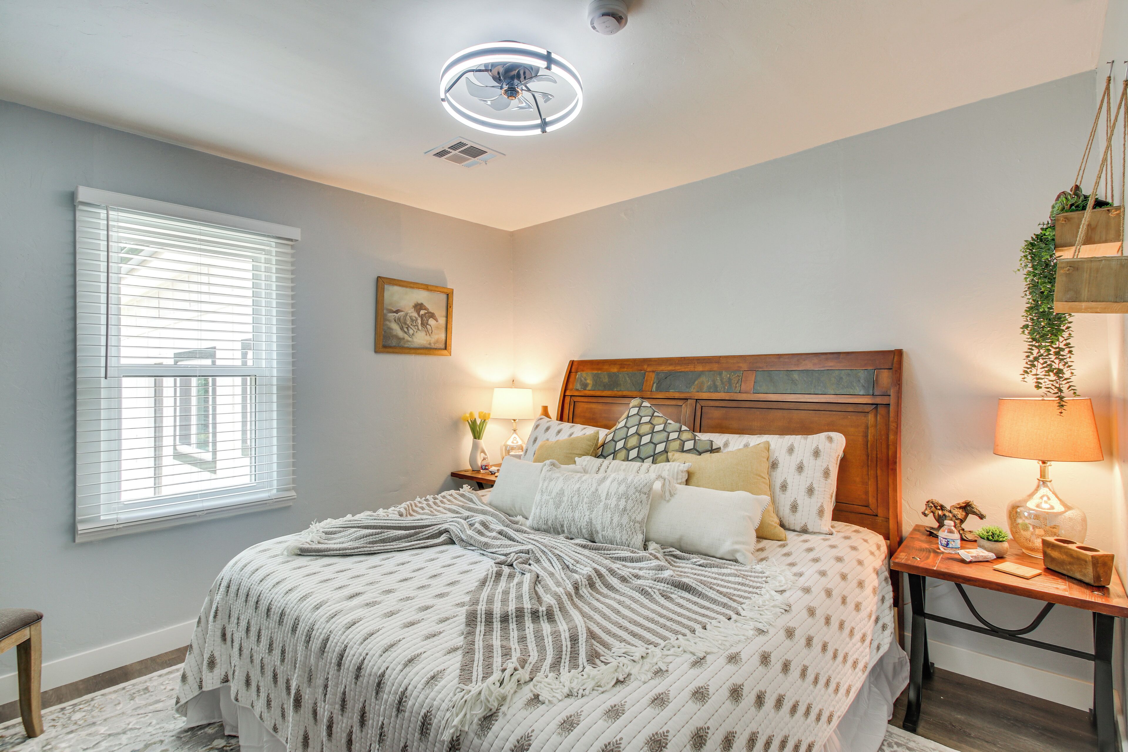 A bedroom with a bed, bedside tables, a nightstand, a ceiling fan, and a window with blinds.