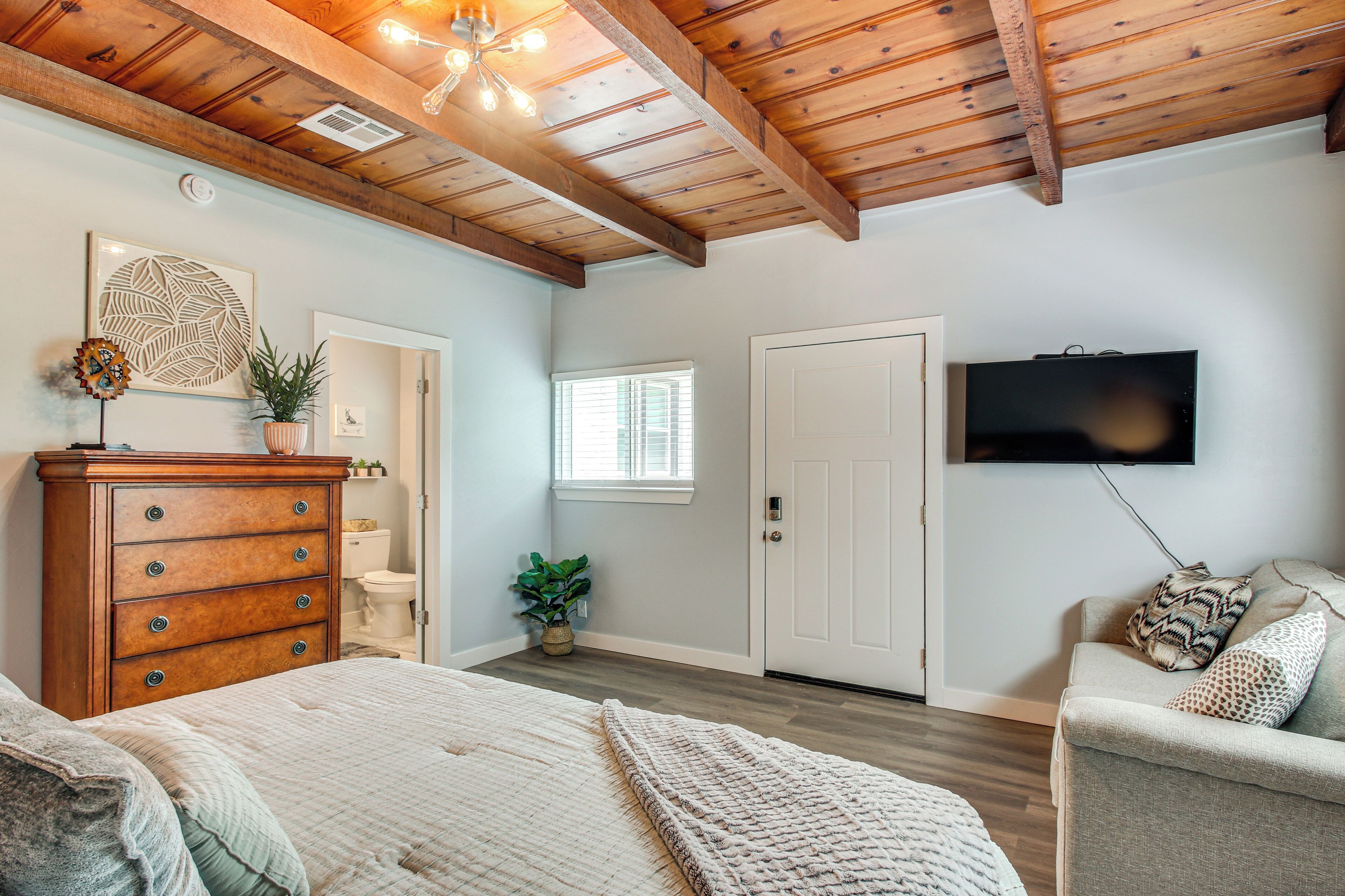 Un dormitorio con techo de madera, una cama con cubrecama blanco, un aparador, un televisor y una puerta.