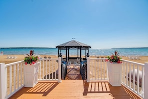 A wooden deck leading to a gazebo on a beach with white railings and potted plants. - Rooftop Deck, Bay Views! Traverse City Penthouse (Traverse City)