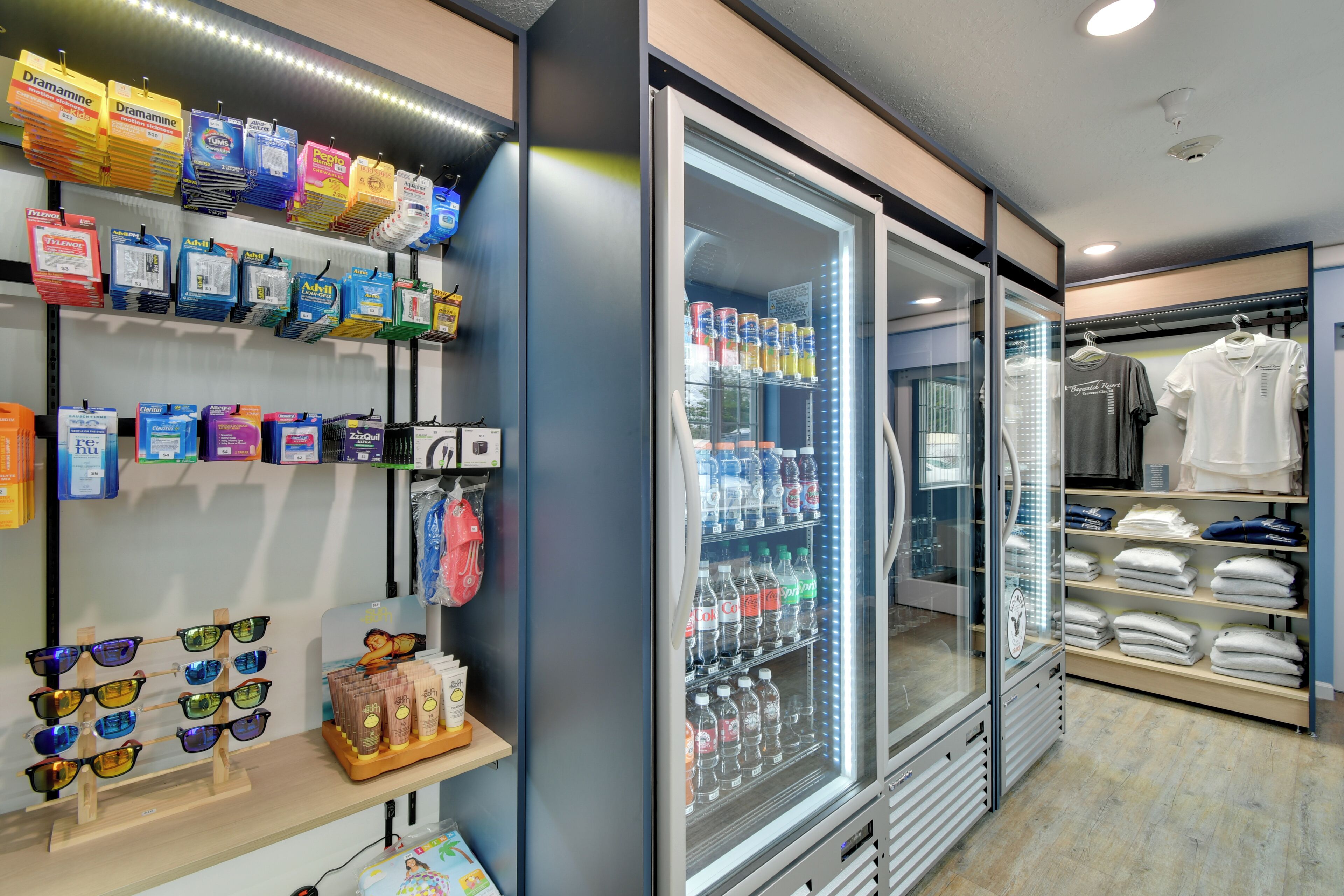 A retail store with shelves of personal care products, a refrigerated display case with beverages, and a clothing rack.