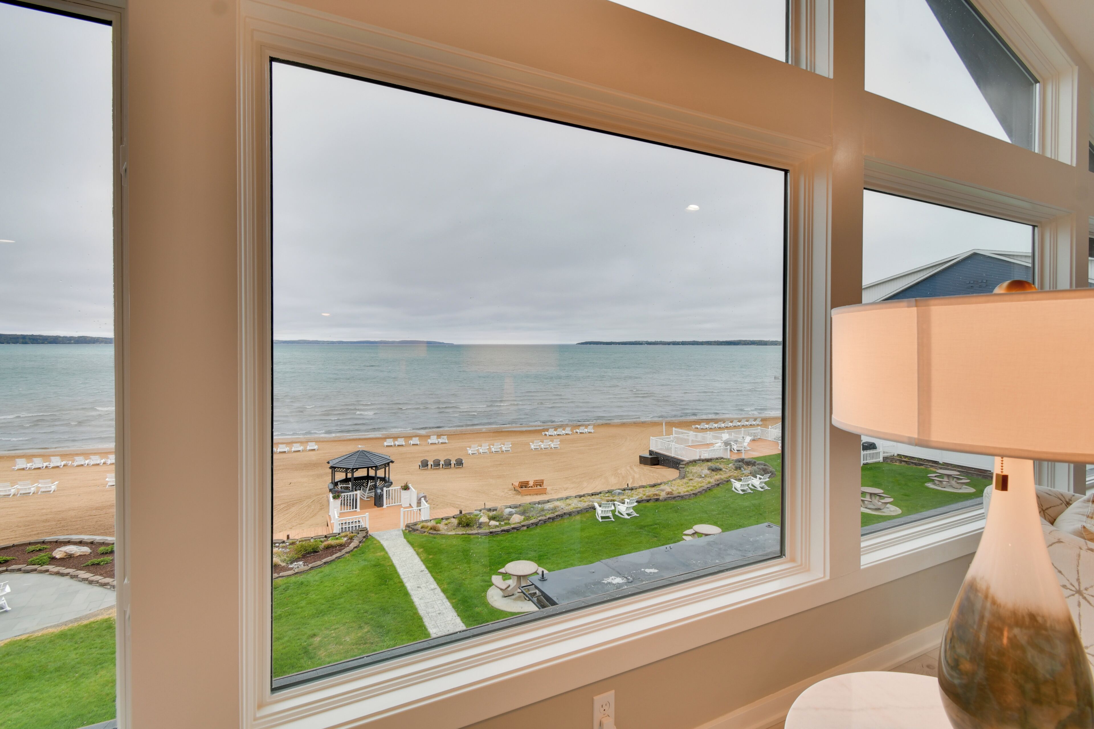 Une pièce dotée d’une grande fenêtre donnant sur une plage, d’une lampe et offrant une vue sur la mer.