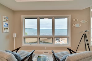 A room with a large window overlooking a beach, two chairs, a telescope, and wall art. - Rooftop Deck, Bay Views! Traverse City Penthouse (Traverse City)