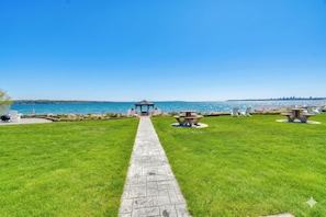 A pathway leading to a gazebo by a body of water, with picnic tables and chairs arranged on the lawn. - Rooftop Deck, Bay Views! Traverse City Penthouse (Traverse City)