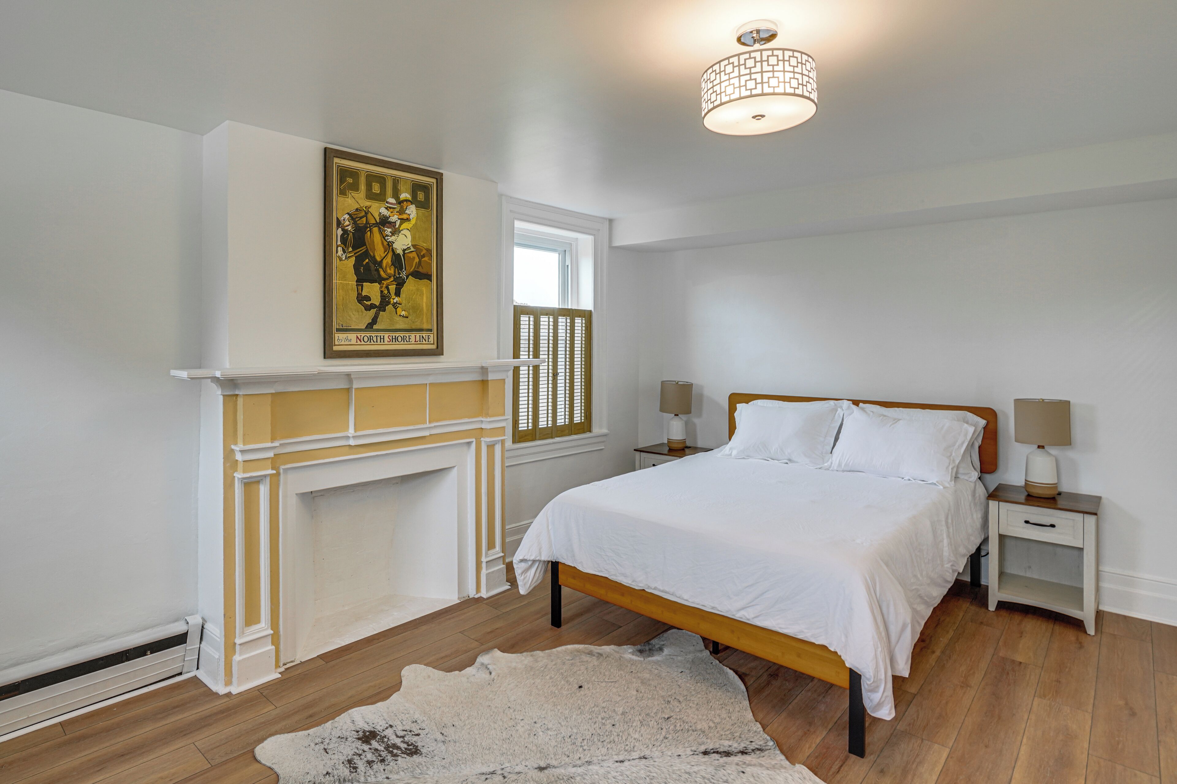 A bedroom with a bed, nightstands, a fireplace, a rug, and a poster on the wall.