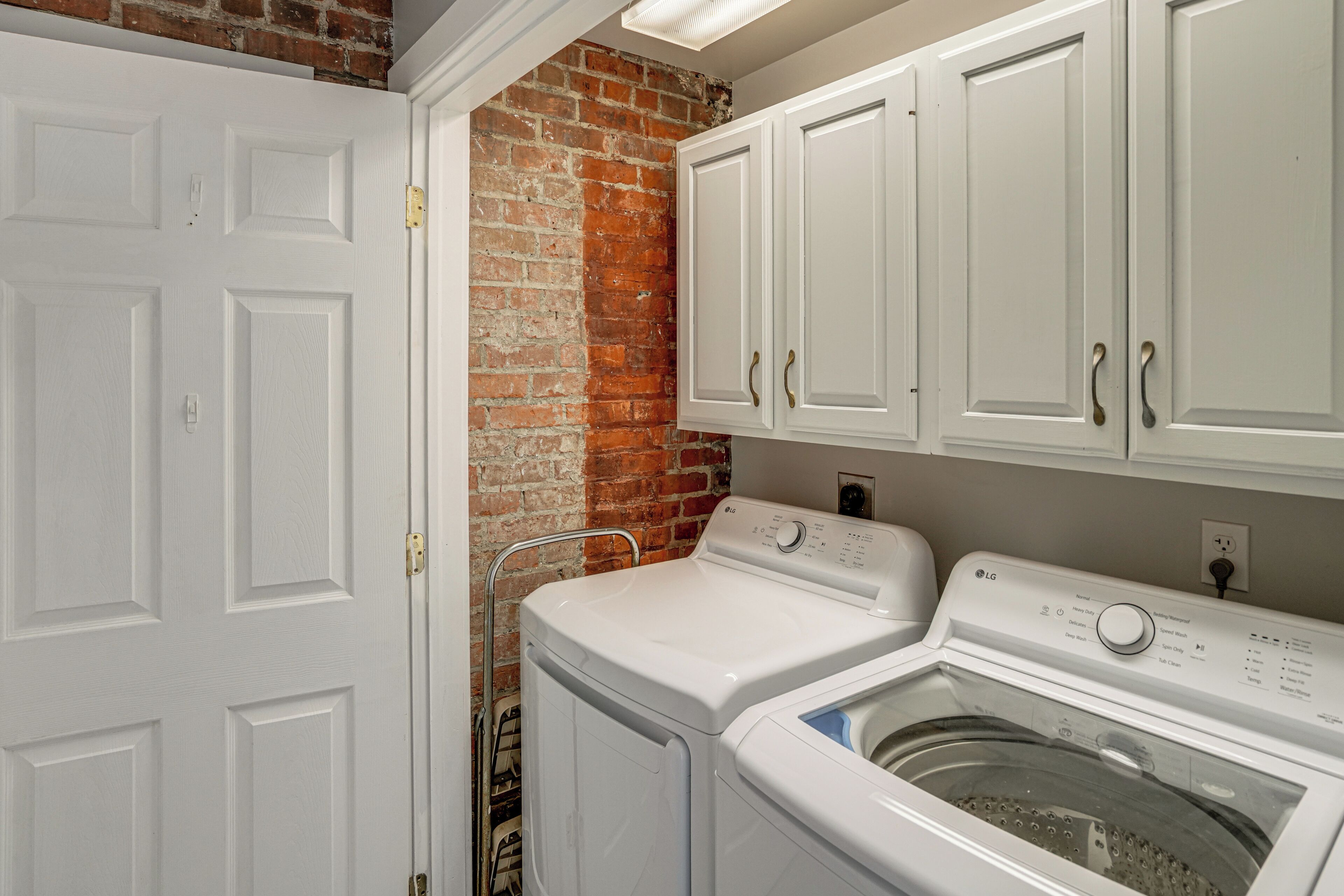 A laundry room with a white door, a brick wall, and white cabinets.