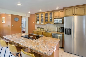Una cocina con encimeras de granito, armarios de madera, un refrigerador de acero inoxidable y un microondas integrado.