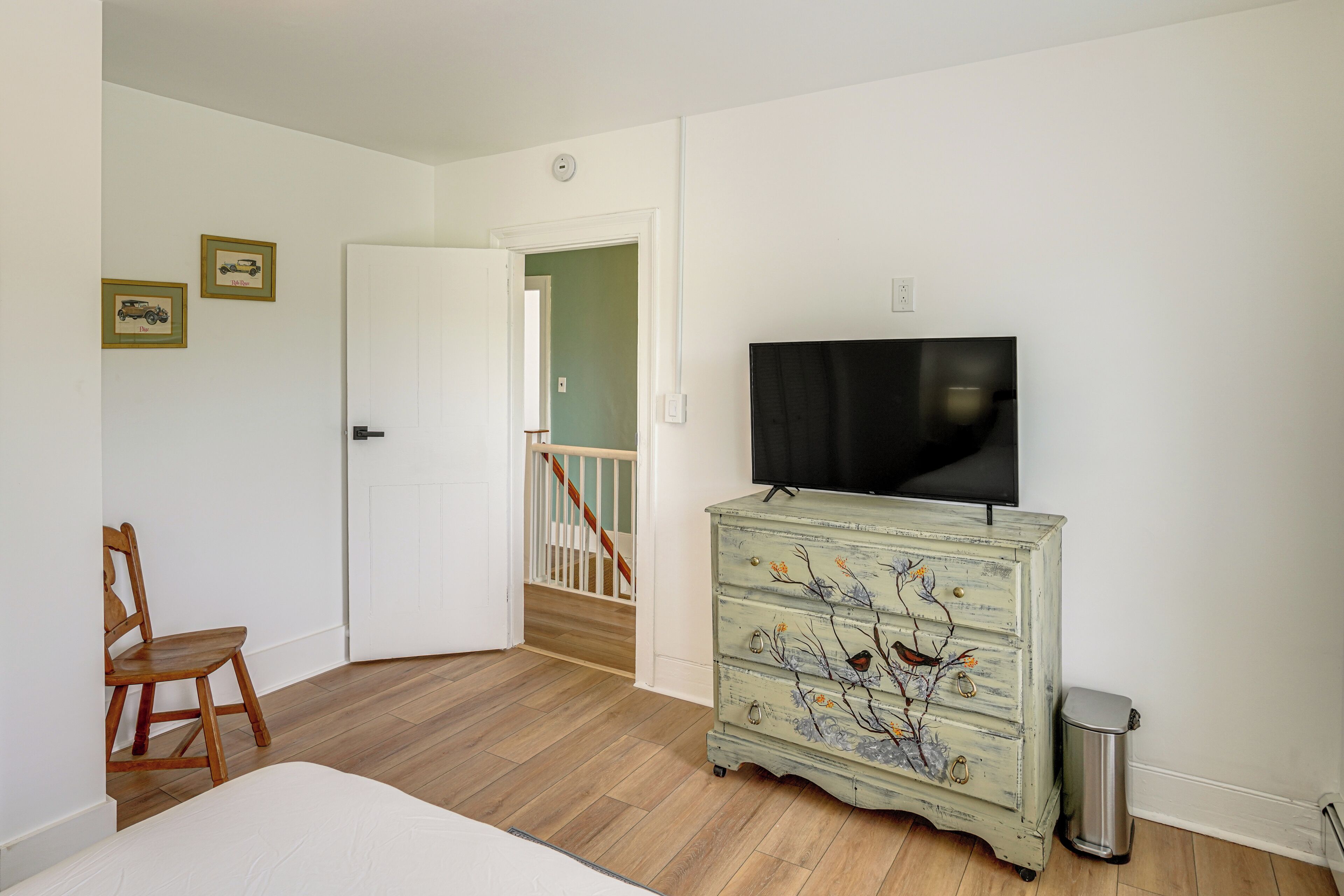 A bedroom with a bed, a dresser, a television, and a door leading to a staircase.