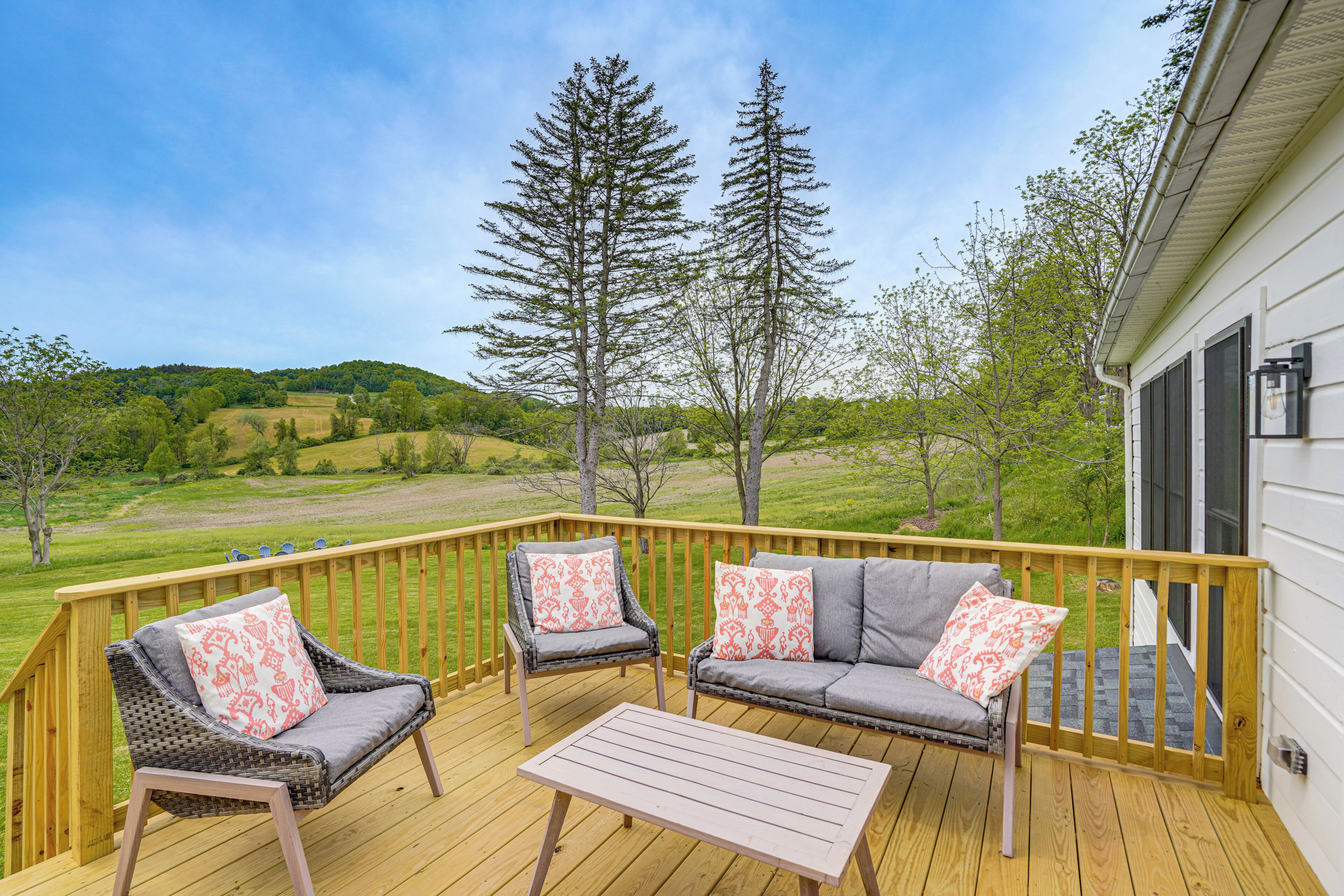 A deck with two chairs and a table, overlooking a green landscape with trees and hills.