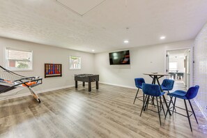 A room with a foosball table, a television mounted on the wall, and a seating area with chairs. - Easy Access to Dtwn & Fort Benning: Family Home (Columbus)