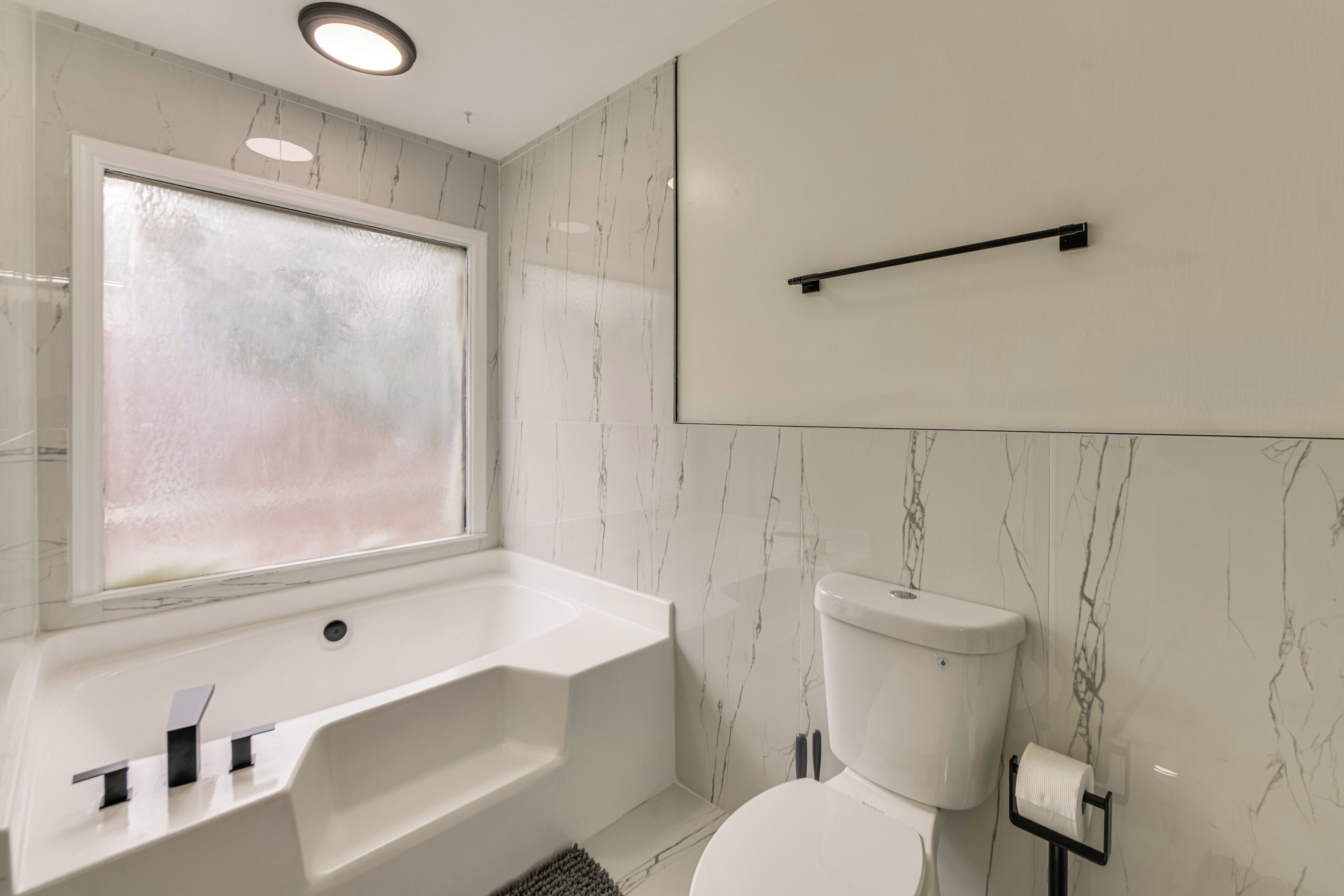 Een moderne badkamer met een bad, toilet en een raam.