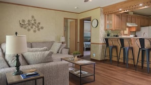 A living room with a sofa, coffee table, and lamp; a kitchen with wooden cabinets and bar stools; and a hallway with a clock. - Lakeview Legacy~Holmes Bend Marina~Walk to Lake (Columbia)