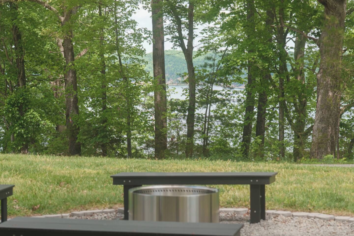 Zona de picnic con una parrilla metálica y bancos, rodeada de árboles y vistas al lago.