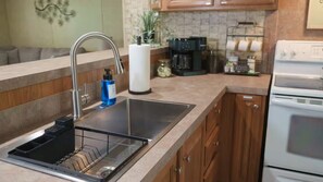 Una cocina con un lavamanos de acero inoxidable, una cafetera y armarios de madera.