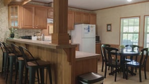 A kitchen with wooden cabinets, a refrigerator, a bar area with stools, and a dining table with chairs. - Lakeview Legacy~Holmes Bend Marina~Walk to Lake (Columbia)