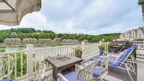 Eine Terrasse mit Gartenmöbeln, einem Feuerkorb und Blick auf einen Fluss und Gebäude.