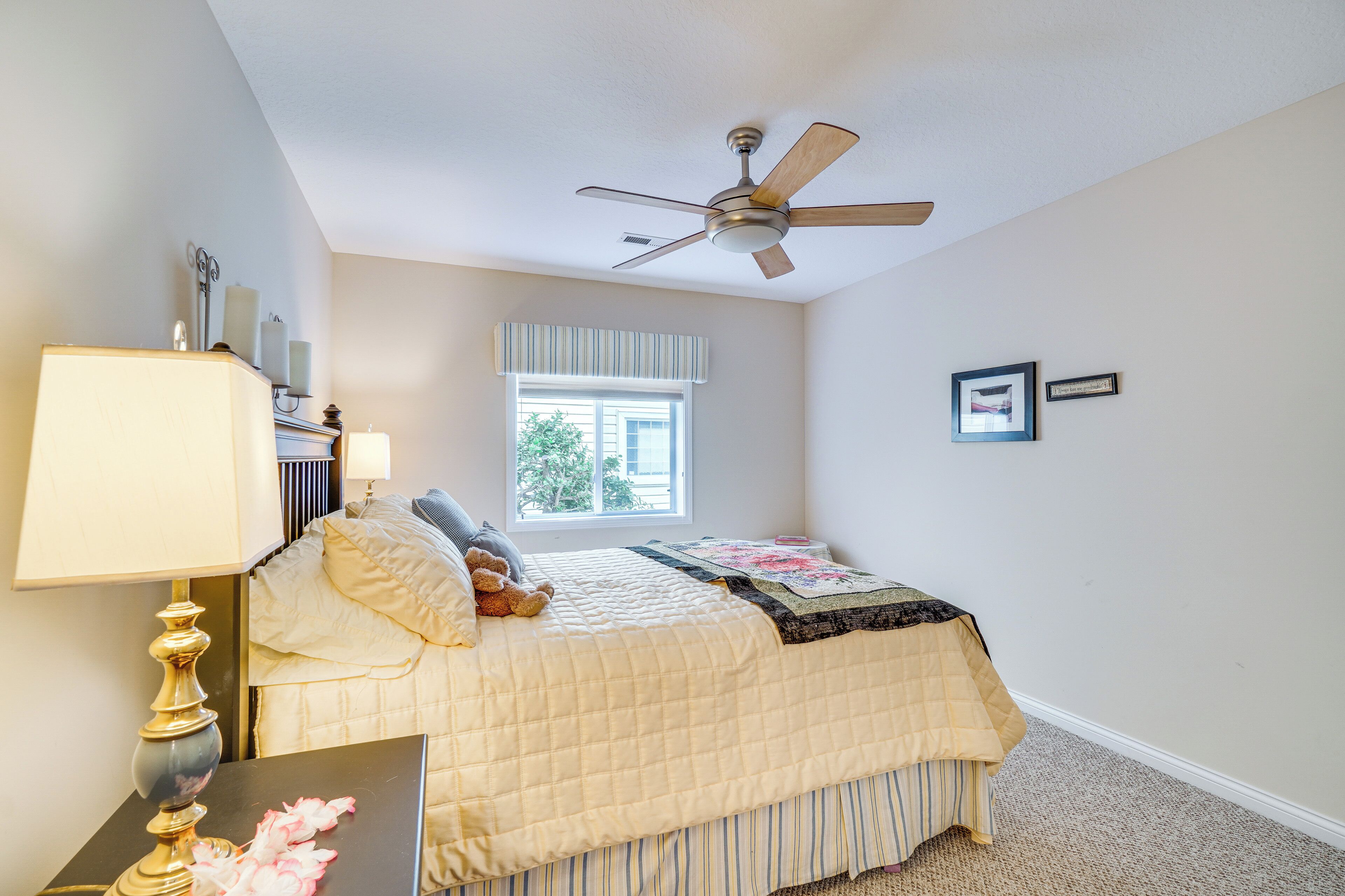 A bedroom with a bed, a ceiling fan, a window, and a bedside table with a lamp.