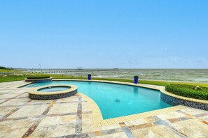 A swimming pool with a curved design, surrounded by a tiled deck and a view of the sea.