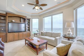A spacious living room with a large flat-screen TV, a wooden coffee table, a beige sofa, and a view of the ocean through large windows. - Bayfront Villa w/ Million-dollar Views in Seabrook (Seabrook)