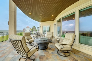 A covered outdoor seating area with a round table, chairs, and a view of the ocean.