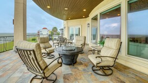 A covered patio area with outdoor furniture, a round table, and large windows offering views of the surrounding landscape. - Bayfront Villa w/ Million-dollar Views in Seabrook (Seabrook)