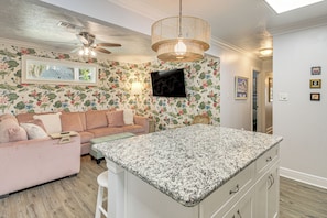Una cocina con encimera de granito, ventilador de techo, televisor montado en la pared y un diseño de papel tapiz floral.