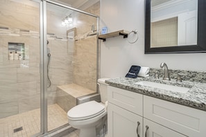 Een moderne badkamer met een douche met glazen wand, een wit toilet, een wastafel met granieten blad en een spiegel boven de wastafel.