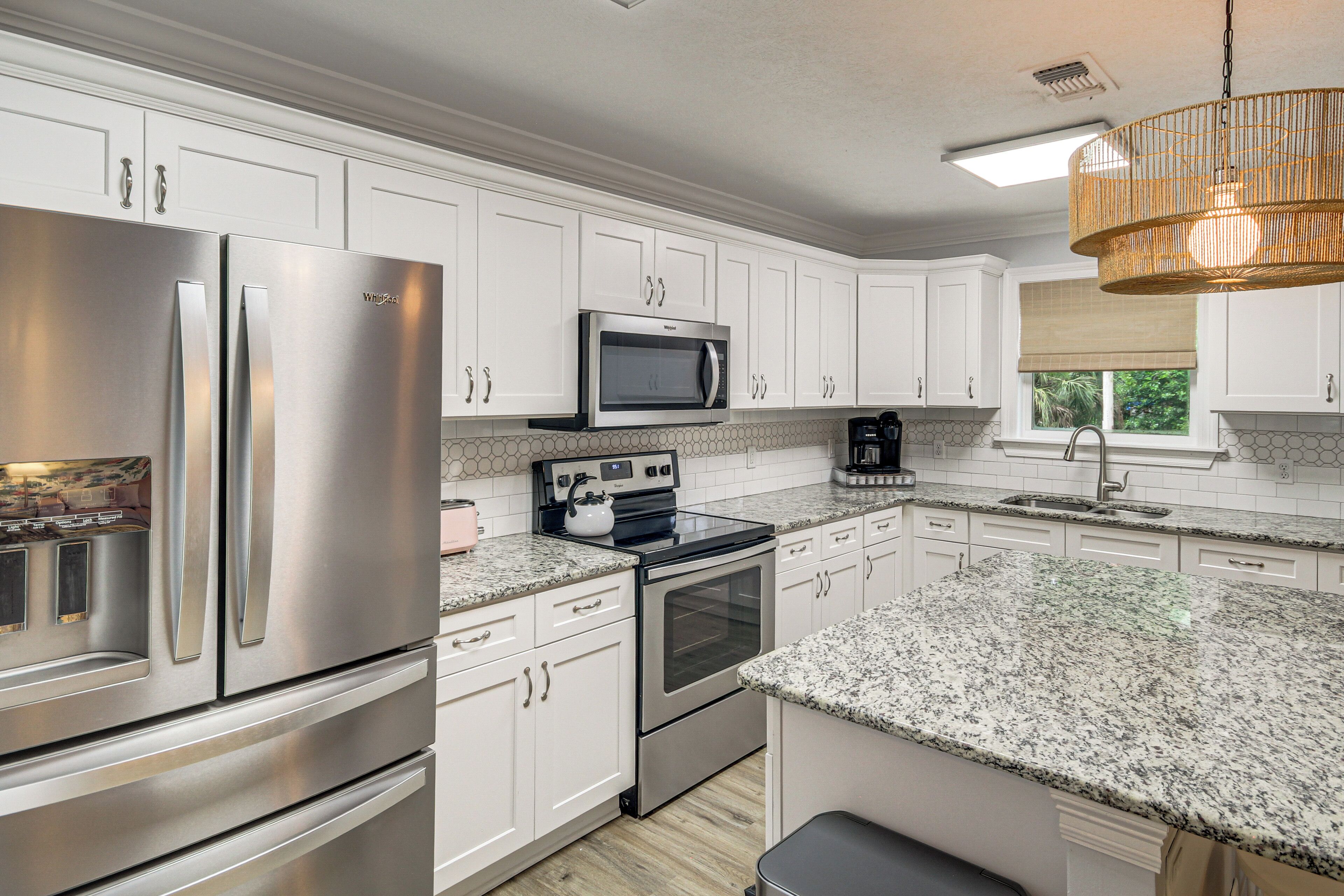 A modern kitchen with stainless steel appliances, white cabinetry, granite countertops, and a hanging light fixture.