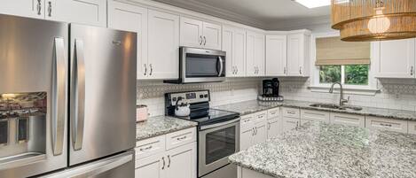 A modern kitchen with stainless steel appliances, white cabinetry, granite countertops, and a hanging light fixture.