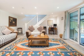 Ein Wohnzimmer mit einer Couch, einem Couchtisch, einem Teppich mit Muster, einer Treppe und einem Schreibtisch mit einem Computer.