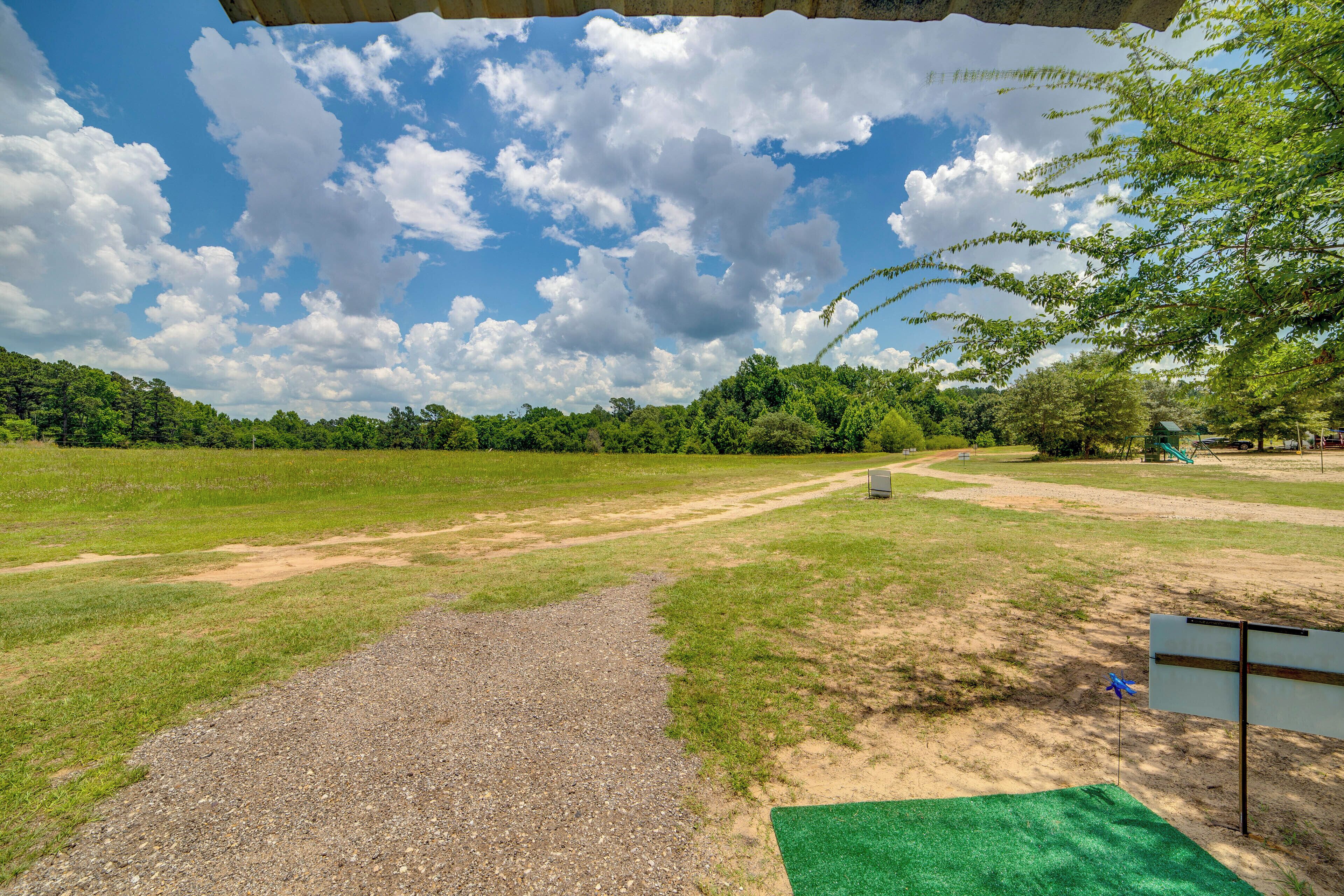 A park with a gravel path, green grass, and trees under a partly cloudy sky.