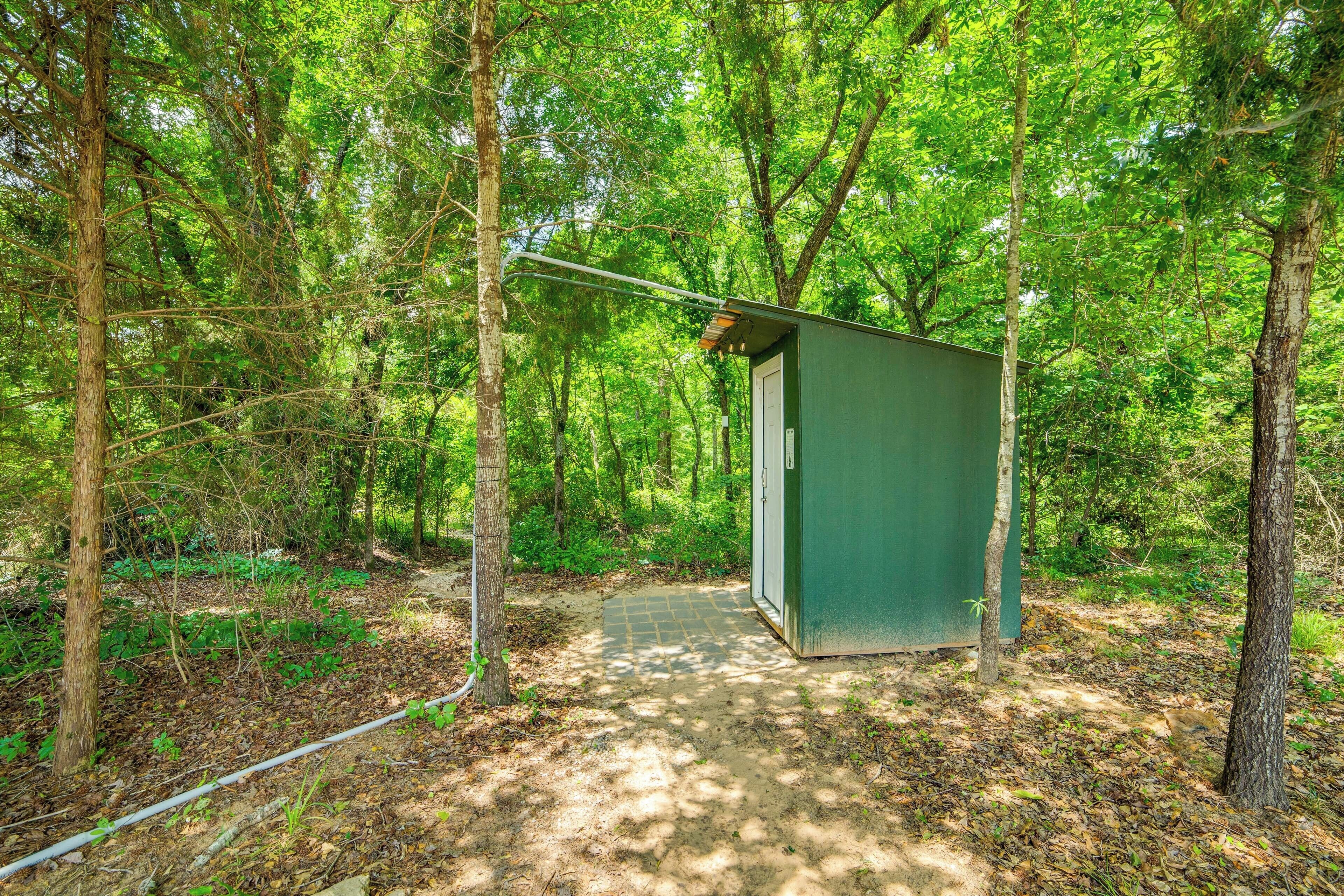 Una pequeña construcción verde de una sola habitación en un área boscosa, con un sendero de tierra que la lleva a ella.