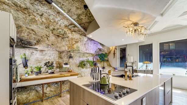 Una cocina moderna con una isla central, pared de piedra y una lámpara de araña.