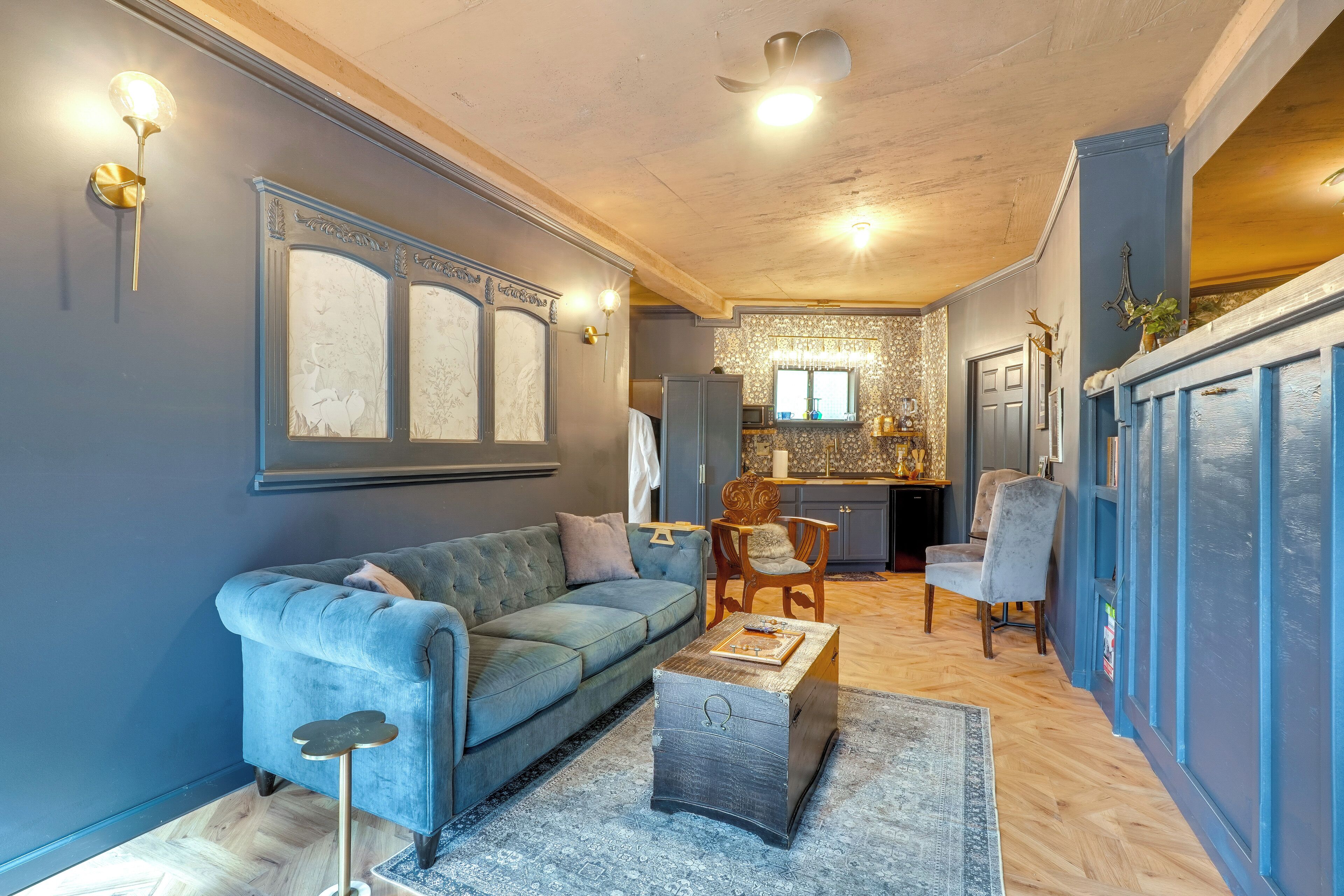 Un salon avec un canapé bleu, une table basse et un tapis. Il y a également un coin cuisine avec une fenêtre et une porte.