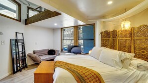 Un dormitorio con una cama, un banco de madera, un sofá, un televisor y un ventanal grande.