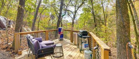 A wooden deck with a grill, a barbecue, and a seating area with a chair and cushions.